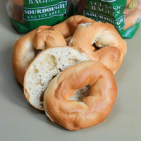 Bagels with one sliced open on a gray surface, with 'Classic Bagels' packaging in the background.