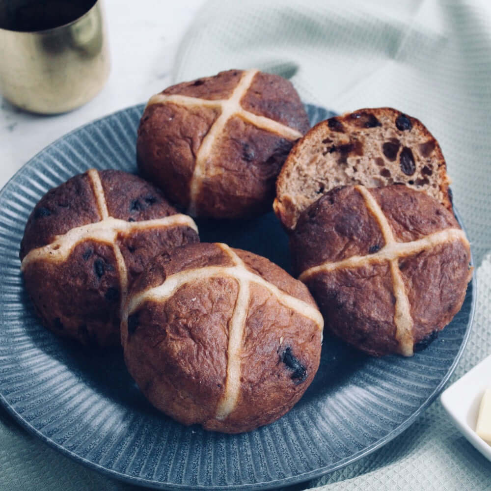 A plate containing four gluten-free hot cross buns with a cross-shaped top, baked and ready to eat.